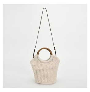 Detailed view of cream woven tote featuring round wooden handles and a black shoulder strap