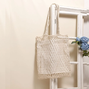 White handwoven mesh tote bag with inner pouch hanging on a vintage wooden window frame
