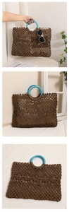 Detail of hollow woven straw bag featuring blue round handles and brown crochet patterns