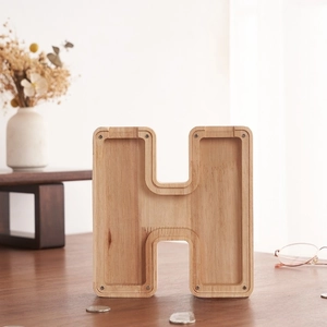 Detalle de la hucha de madera en forma de H con panel acrílico sobre un escritorio