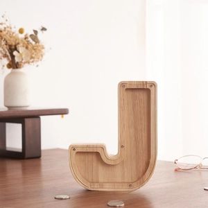 Detalle de una hucha de madera en forma de J con panel acrílico sobre una mesa de madera