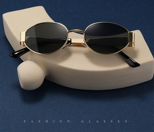 Detail view of oval metal sunglasses with gold frames and dark lenses on a blue background