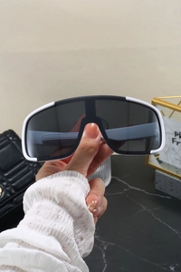 Detail of white cycling sunglasses with dark grey lenses held over a stylish background