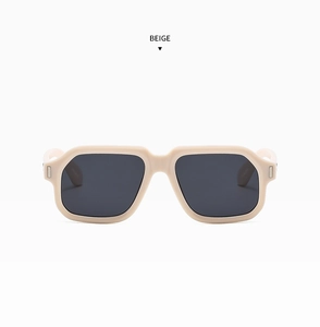 Detail of beige rectangular sunglasses featuring silver metal rivets and dark grey lenses