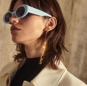 Close-up of light blue oval sunglasses and long gold palm tree letter earrings