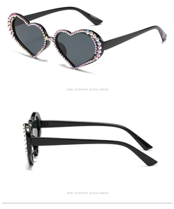 Detail view of heart-shaped sunglasses featuring rainbow rhinestones on black frames