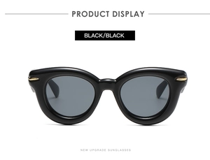 Detail view of oval sunglasses with thick black frames and golden metal temple accents