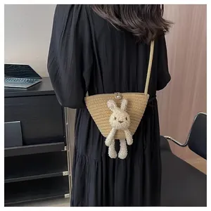 Détail d'un sac bandoulière en paille tressée avec lapin en peluche porté sur mannequin