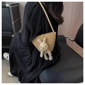 Gros plan d'un sac seau lapin tissé beige porté à l'épaule avec une robe noire élégante