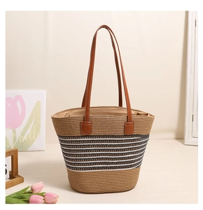 Detail of straw tote bag with black and white woven stripes and brown leather handles