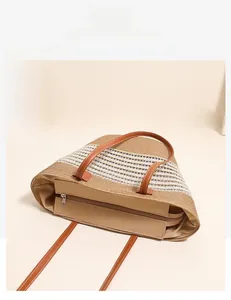 Detail view of large straw tote bag featuring brown leather trim and secure zip closure