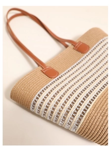 Detail view of woven straw tote bag with white and silver striped pattern and leather handles
