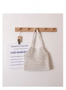 Détail d'un sac cabas au crochet en coton beige évidé suspendu à un crochet en bois