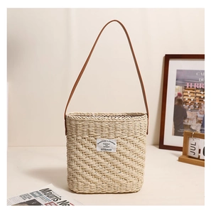 Close-up of a square straw woven shoulder bag with a brown leather strap and brand label