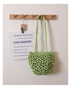 Detail of light green knit tote bag featuring hollow floral pattern on a wood hook