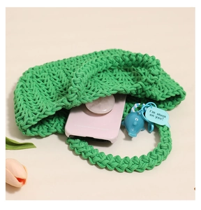 Detail of green knit tote bag with pink phone case inside and blue dolphin charm