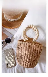 Detail of hand-woven straw bucket bag featuring round wooden bead handles and leather accents