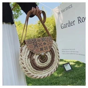 Detail of round straw bag with geometric patchwork flap and bronze metal lock on grass