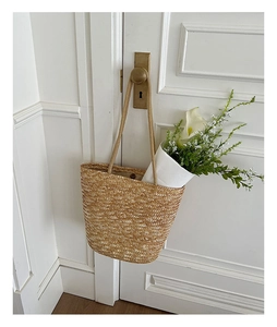 Detail of straw woven tote bag with natural texture, brass buckle and flowers on a white door