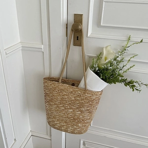 Handmade straw tote bag with long straps hanging on a white door with calla lilies