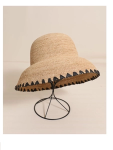 Detail of raffia sun hat with woven texture and black fringe trim on a stand