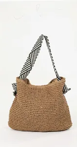 Detail of hand-woven straw shoulder bag featuring stylish black and white striped straps