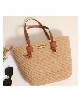 Close-up of woven cotton tote bag featuring brown leather handles and metal logo detail