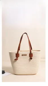 Detail of khaki woven tote bag showing leather handles and rectangular metal logo plaque