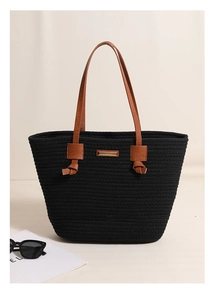 Detail of black woven tote bag featuring brown faux leather straps and a gold metal logo