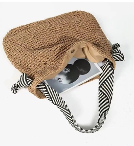 Detail of woven straw shoulder bag with striped fabric strap and magnetic snap closure