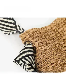 Close-up of woven straw bag with black and white striped strap and metal grommets