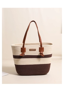 Detail of striped cotton woven tote bag with brown leather handles and metal logo plaque
