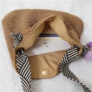Straw shoulder bag with striped ribbon handles and flower charm on white textured background
