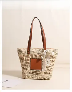 Detailed macro view of beige straw tote bag featuring brown leather patch and lace bow detail