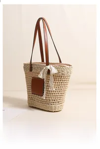 Close-up of khaki straw tote bag featuring leather patch and white lace bow detail
