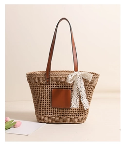 Detail of straw tote bag featuring brown leather handles and a white lace bow accent