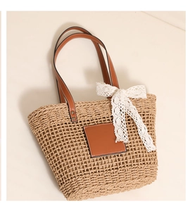 Macro detail of natural straw tote bag featuring leather handles and a lace bow charm