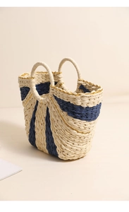 Detail of hand-woven straw tote bag showing navy stripes and gold thread texture