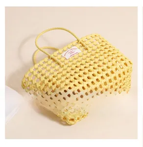Detailed bottom view of a bright yellow hollow woven beach bag with twin handles