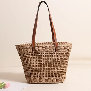 Handwoven straw tote bag with brown leather handles and decorative silk scarf for beach