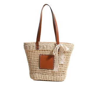 Hollow straw tote bag with brown leather handles and a decorative white lace bow