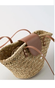 Close-up of straw woven texture with brown leather flap and gold metal rivet details