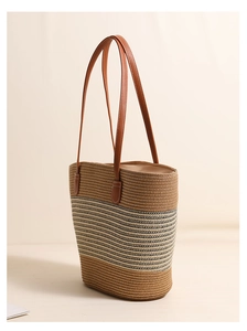 Close-up of a striped woven straw tote bag with brown leather handles and stitching
