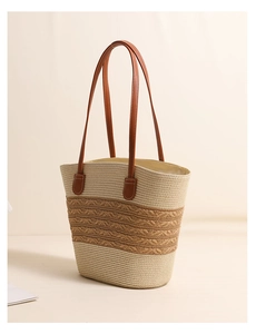Close-up of striped woven straw tote bag featuring premium brown leather handles