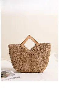 Detail of khaki woven straw handbag with gold thread and square wooden handle on white fabric