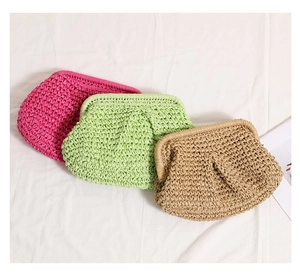 Three colorful woven straw clutch bags in pink, green and tan on a textured fabric