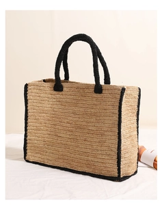 Detail of square raffia tote bag featuring black woven handles and trim for summer beach use