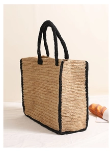 Close-up of the woven texture and black trim on a raffia square straw tote bag