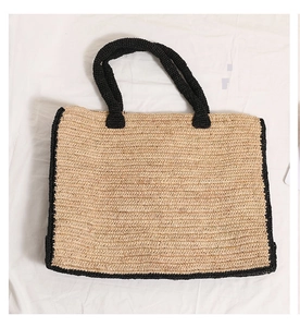 Top view of large straw tote bag with black contrast trim on white wrinkled fabric