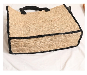 Detailed view of the square raffia straw tote bag base with black woven border accents